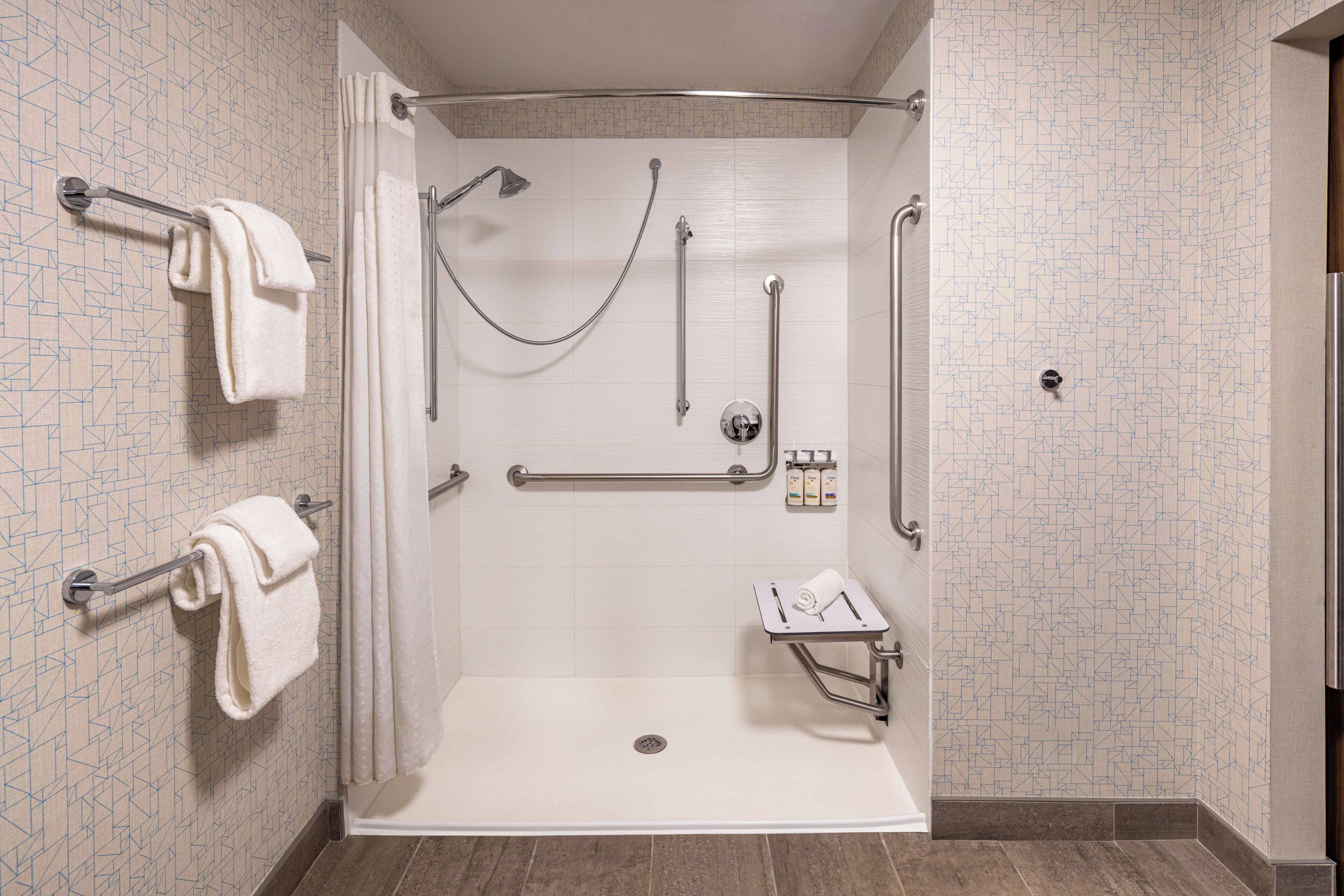 A walk-in shower with a grab bar, a handheld showerhead, and a seat.