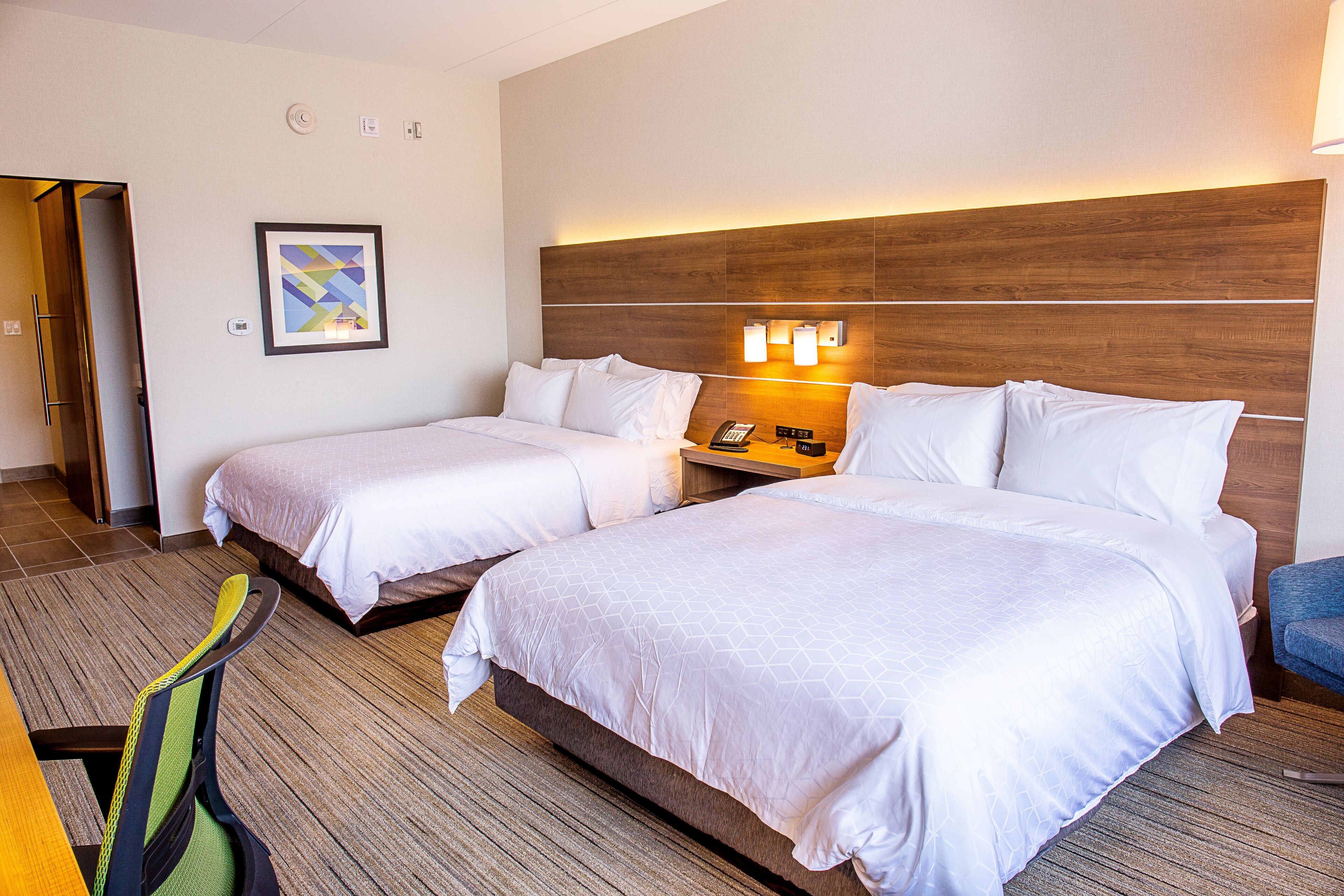 A hotel room with two beds, a desk, and a chair. There is a framed picture on the wall and a phone on the nightstand.