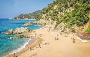 Ein Strand mit klarem, blauem Wasser, Felsformationen und einer bewaldeten Hügelside.