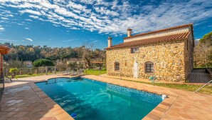 Una casa in pietra con piscina, circondata da un giardino recintato e un paesaggio collinare.
