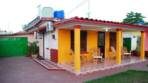 A small, single-story house with a red-tiled roof and a porch with wooden chairs. - Casa Lourdes y Juan Jose (Viñales)