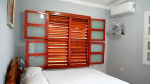 A bedroom with a bed, a wall-mounted fan, and a window with wooden blinds. - Casa Lourdes y Juan Jose (Viñales)