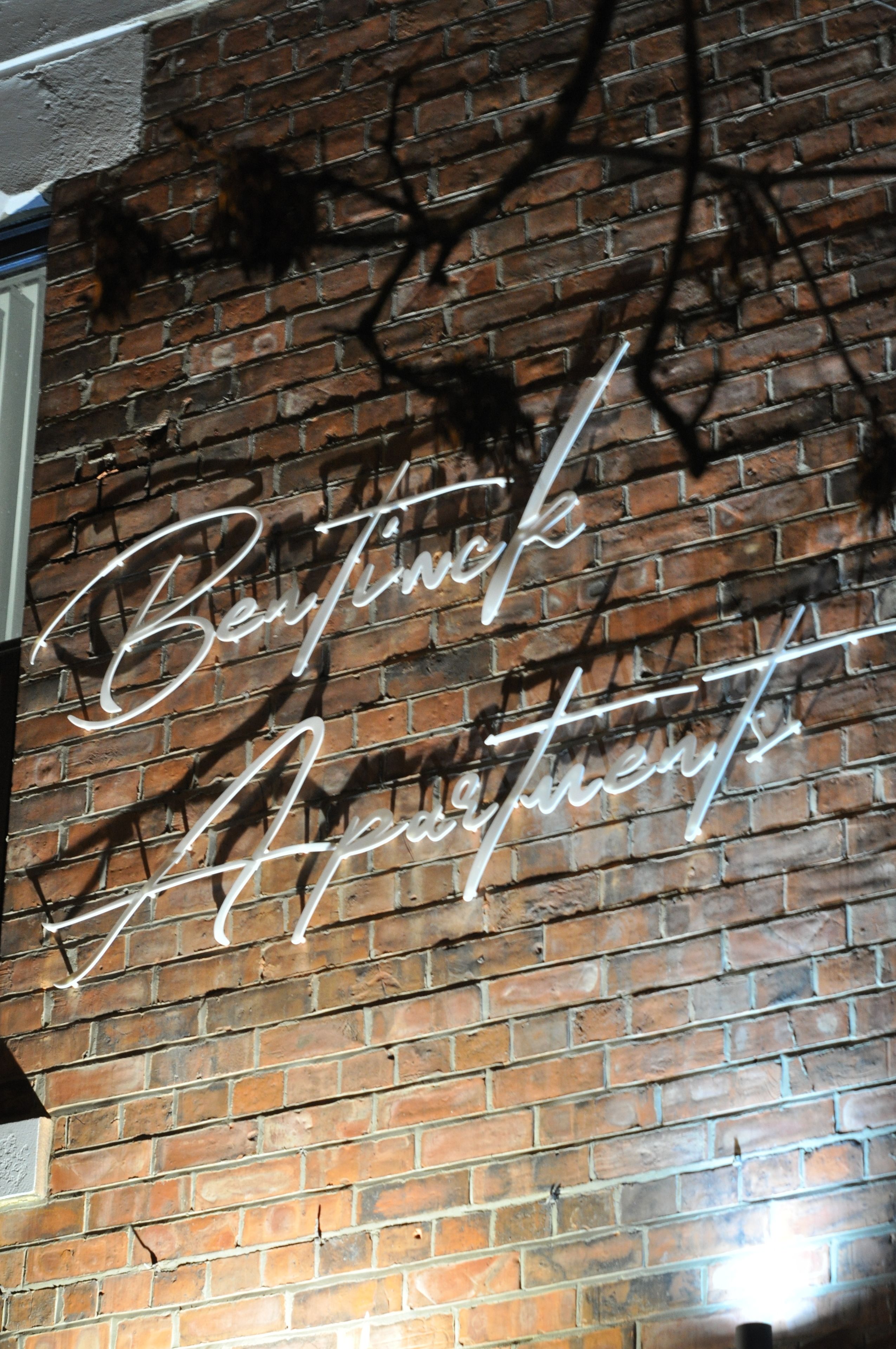 A brick wall with a neon sign spelling "Bennington Apartments."