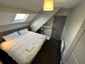 A bedroom with a bed, a nightstand, a desk, a door, and a window. - Bentinck Apartments (Newcastle-upon-Tyne)