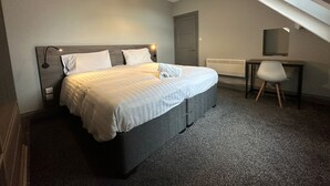 Moderni hotellihuone, jossa on suuri sänky, työpöytä ja tuoli.