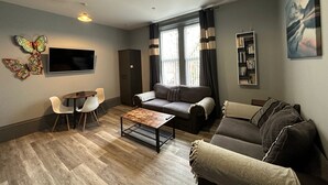 Moderni olohuone, jossa on sohva, sohvapöytä, televisio ja kirjahylly.