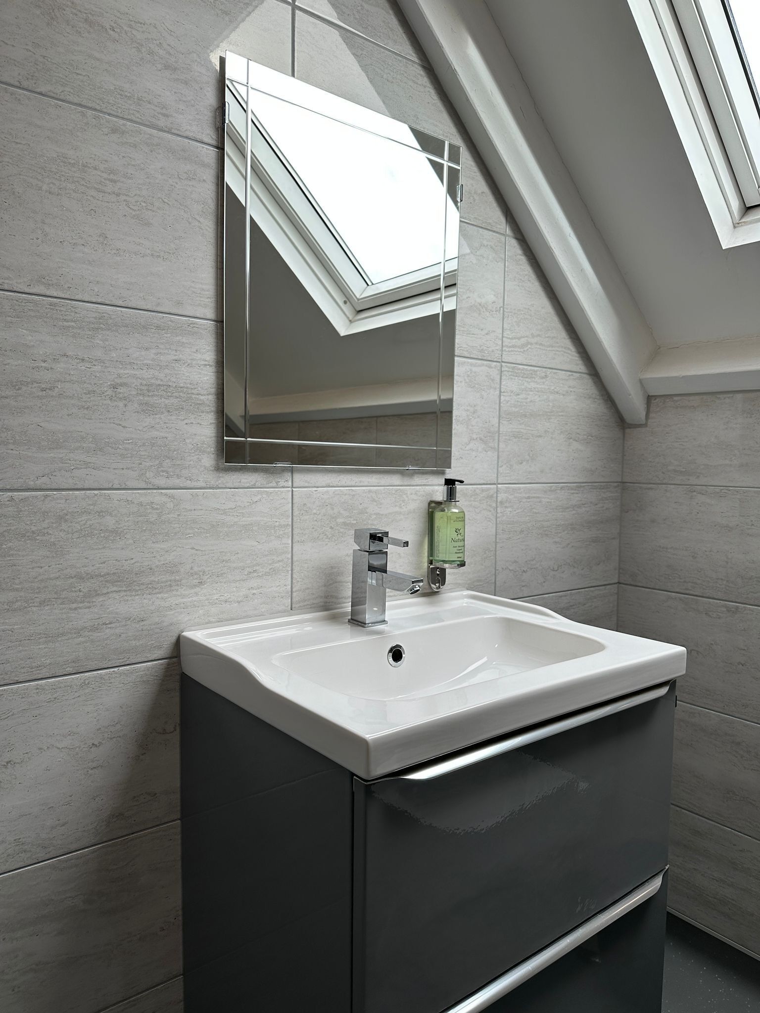 Une salle de bain moderne avec une lucarne, un lavabo blanc et un miroir.