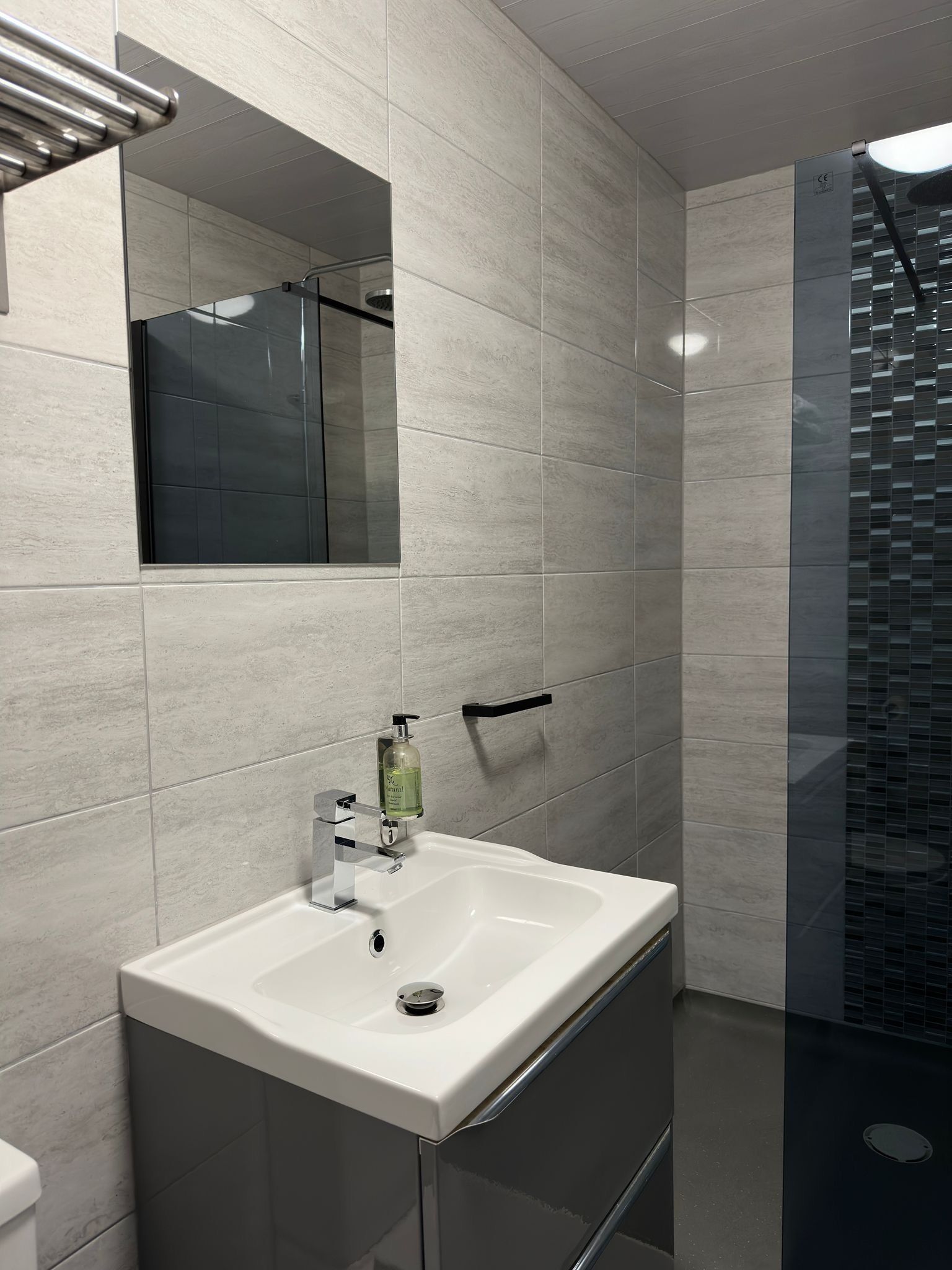 A modern bathroom with a white sink, a mirror, and a shower area.