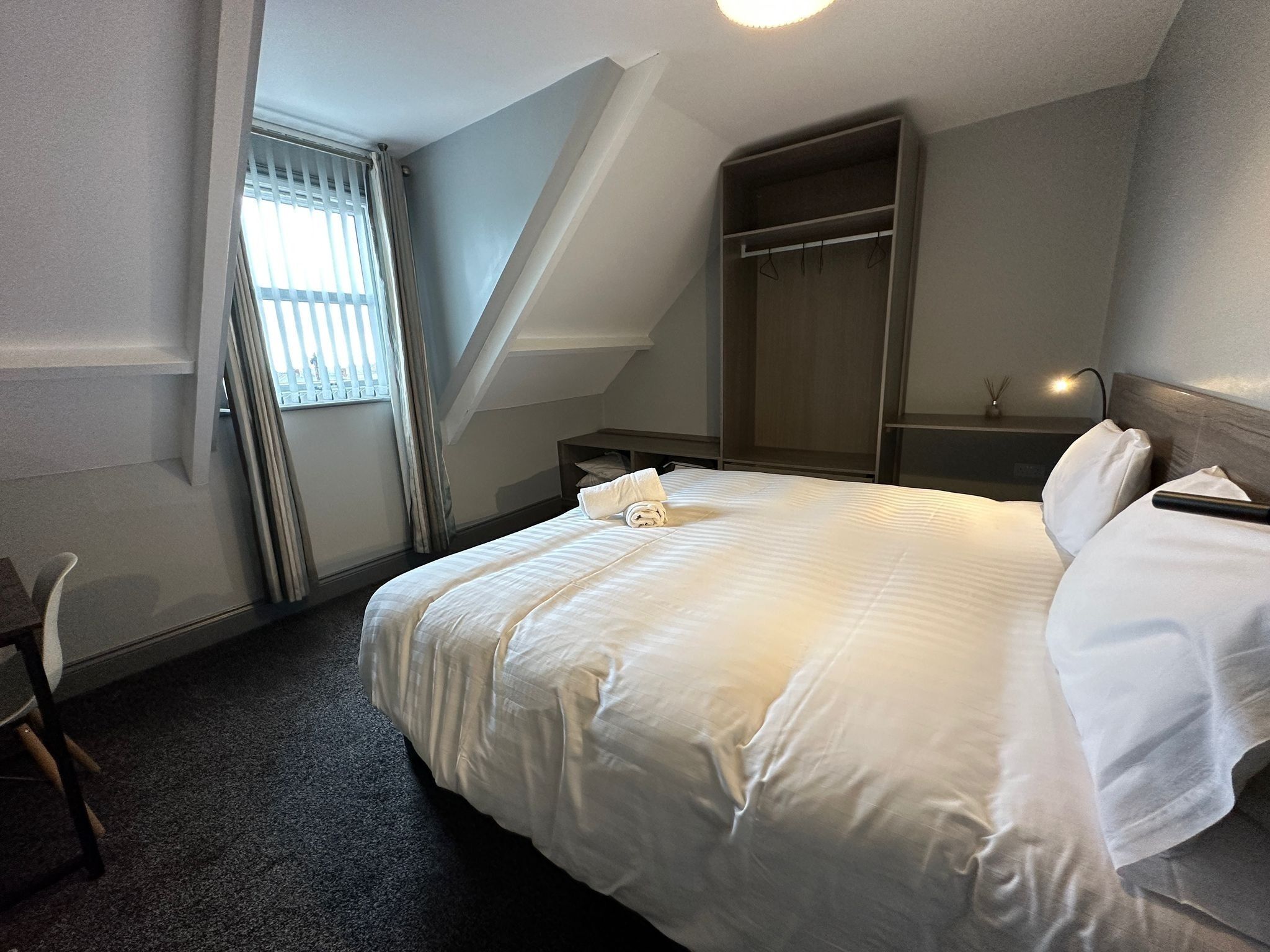 Ett hotellrum med en väl bäddad säng, ett skrivbord och en garderob.