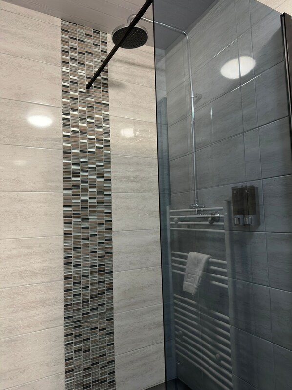 A modern shower with a glass door and a tiled wall.
