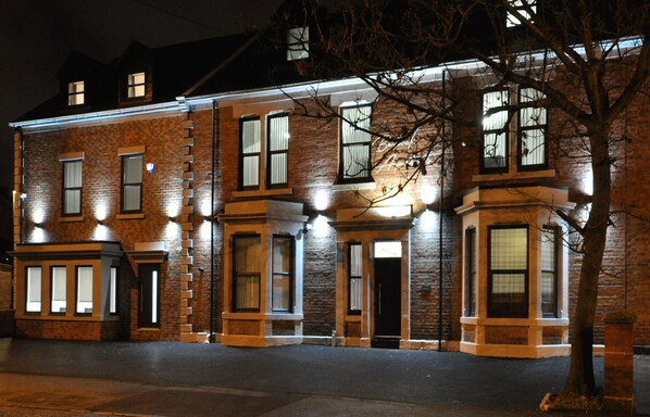 A brick building with multiple windows and doors, illuminated by exterior lighting. - Bentinck Apartments (Newcastle-upon-Tyne)