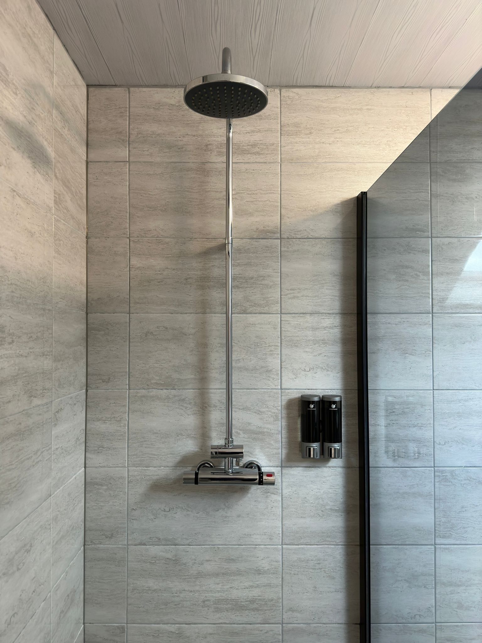 A modern shower with a rain showerhead, a handheld showerhead, and a wall-mounted control panel.