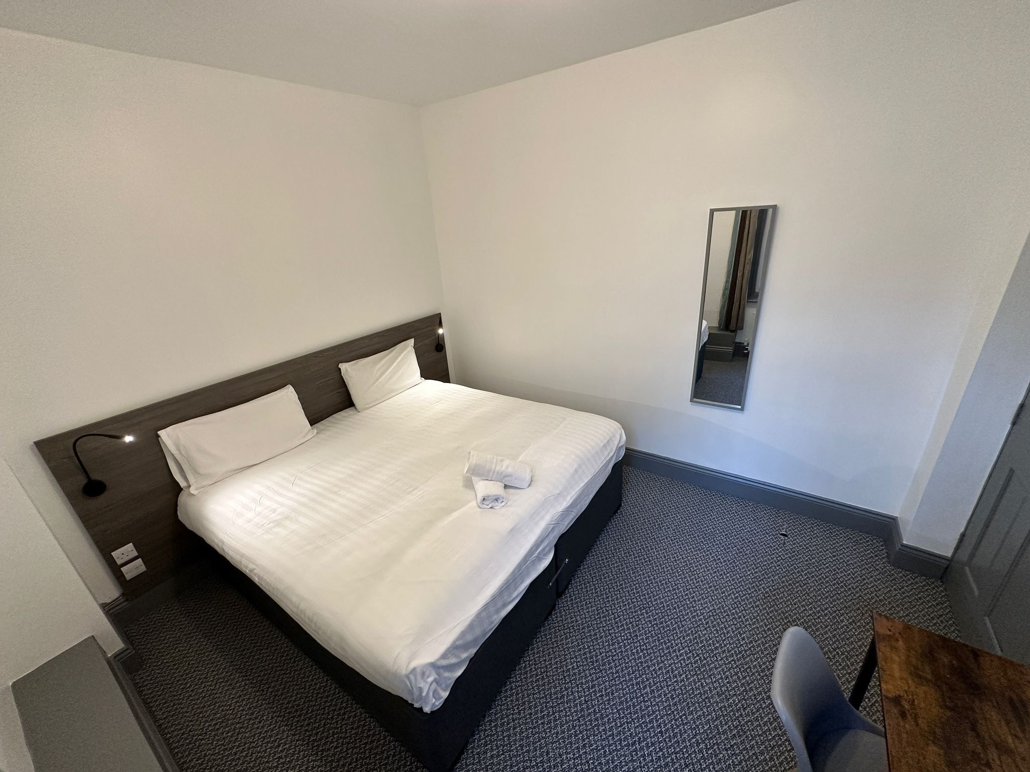 Een hotelkamer met een opgemaakt bed, een tafeltje en een spiegel aan de muur.
