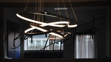 A modern chandelier with a circular design, a window with a view of buildings, and a handwritten sign on the window.