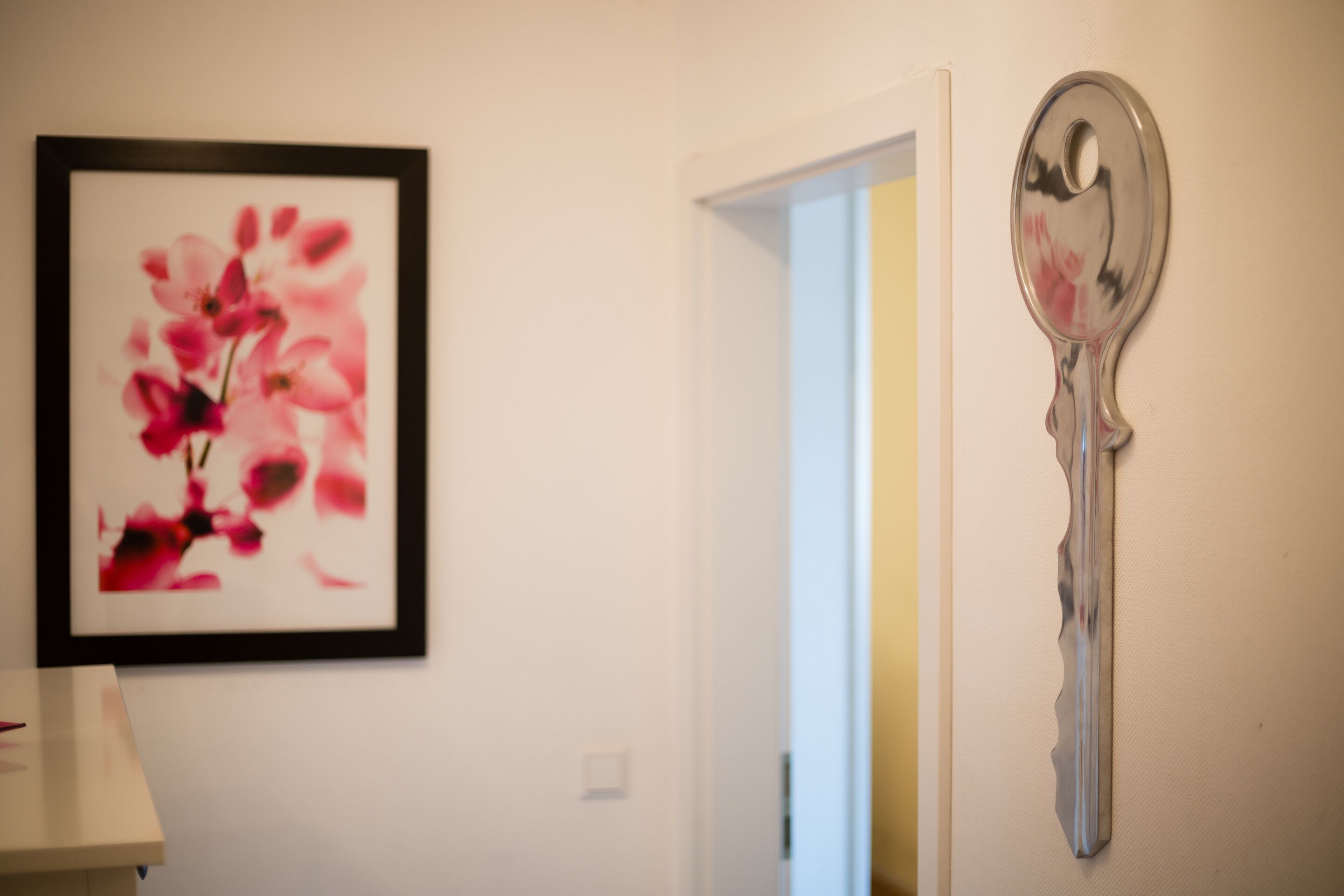 A hallway with a framed floral artwork on the left and a key-shaped mirror on the right.