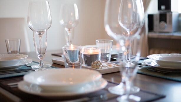 Une table à manger dressée avec des assiettes, des verres et des bougies, ce qui laisse supposer un repas formel.