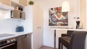 Une cuisine moderne équipée d’un four à micro-ondes, d’un grille-pain et d’un lave-vaisselle encastrés. On y trouve une table à manger avec des chaises et un luminaire suspendu.