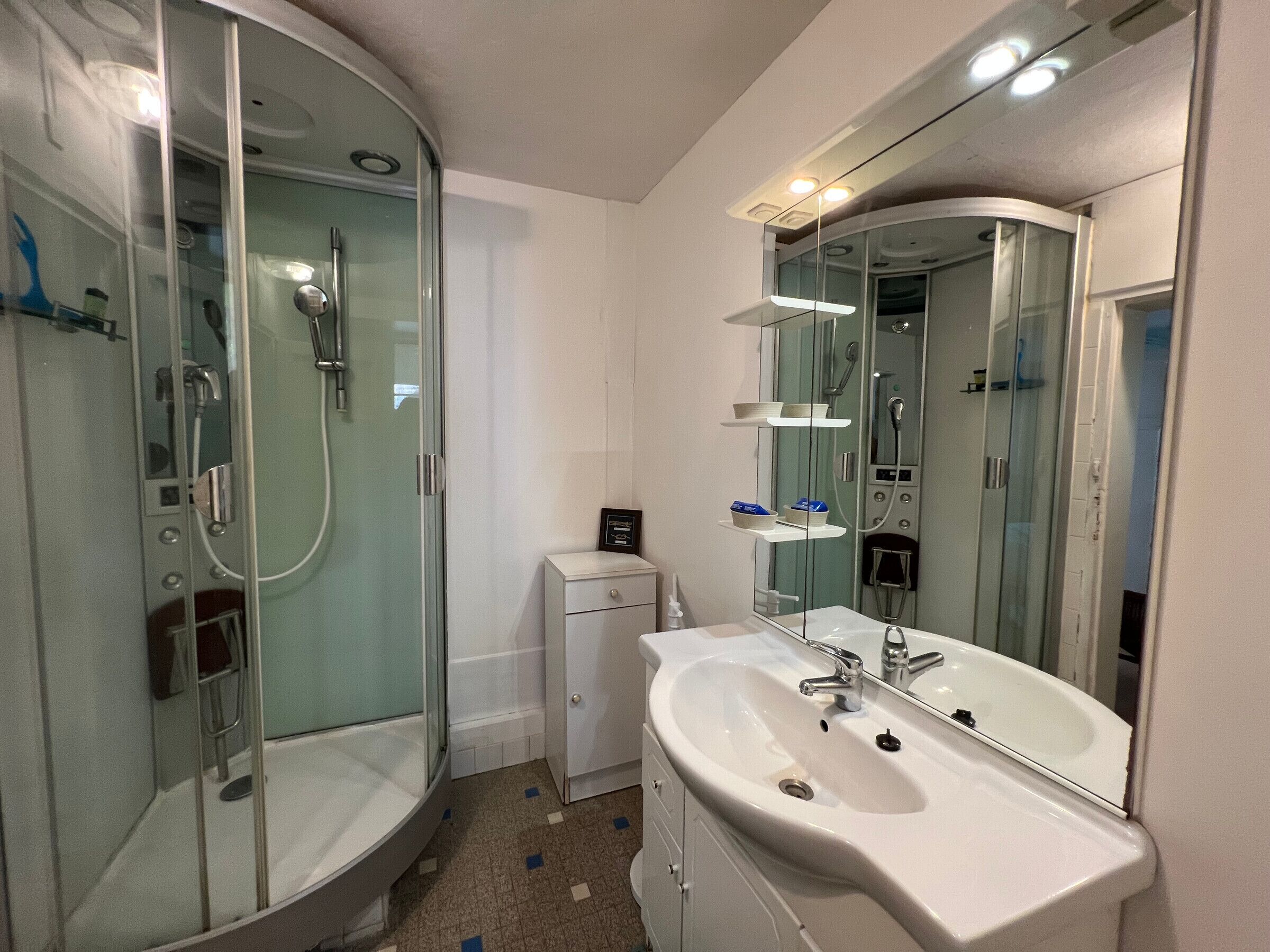 A modern bathroom with a glass-enclosed shower, a white sink, and a large mirror.