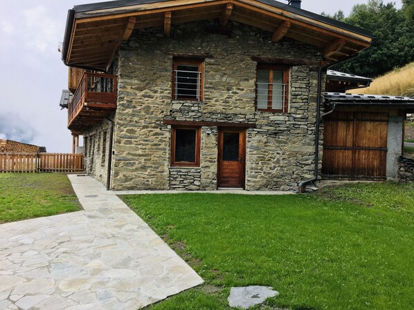 A stone house with a wooden balcony, a stone pathway, and a grassy yard.