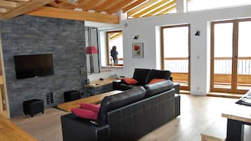 Un soggiorno moderno con parete in pietra, divano in pelle nera, travi in legno al soffitto e televisore a schermo piatto.