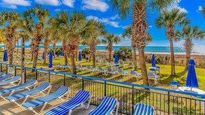 Un complexe hôtelier situé en bord de mer, doté de chaises longues, de palmiers et offrant une vue sur l’océan.