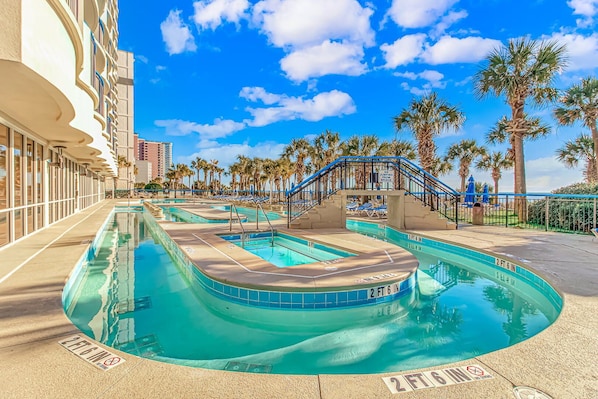A pool area with multiple swimming pools, palm trees, and a bridge.