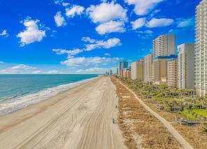 A beach with a long sandy shore, adjacent high-rise buildings, and a clear blue sky.
