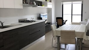 Une cuisine moderne avec des meubles de couleur bois foncé, un îlot central et un coin repas comprenant une table et des chaises blanches.
