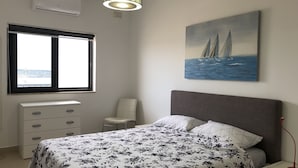 Une chambre à coucher comprenant un lit, une chaise, un bureau, une fenêtre et un tableau représentant des voiliers.
