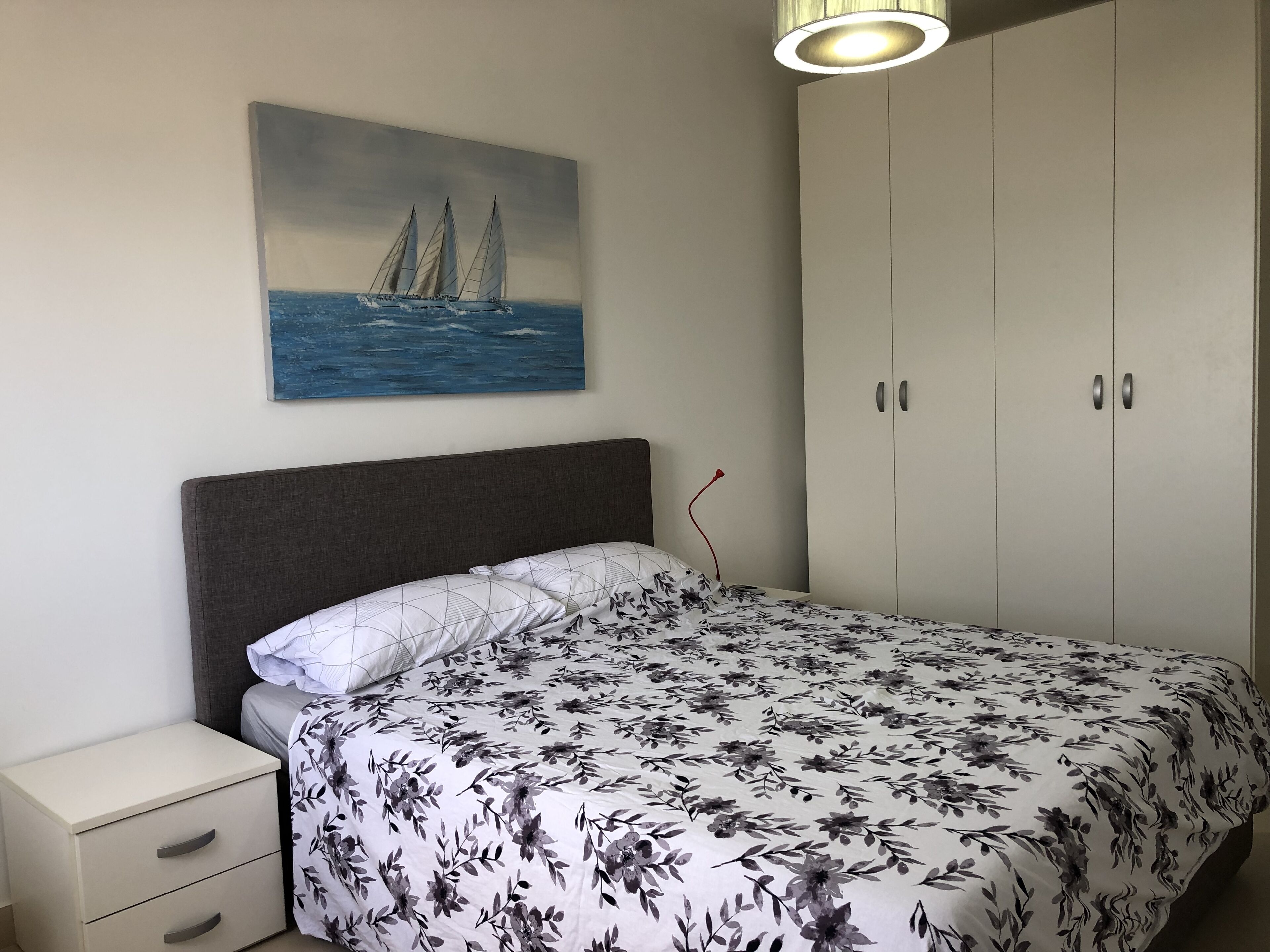Ein Schlafzimmer mit Bett, Nachttisch, Kleiderschrank und einem Gemälde eines Segelboots an der Wand.