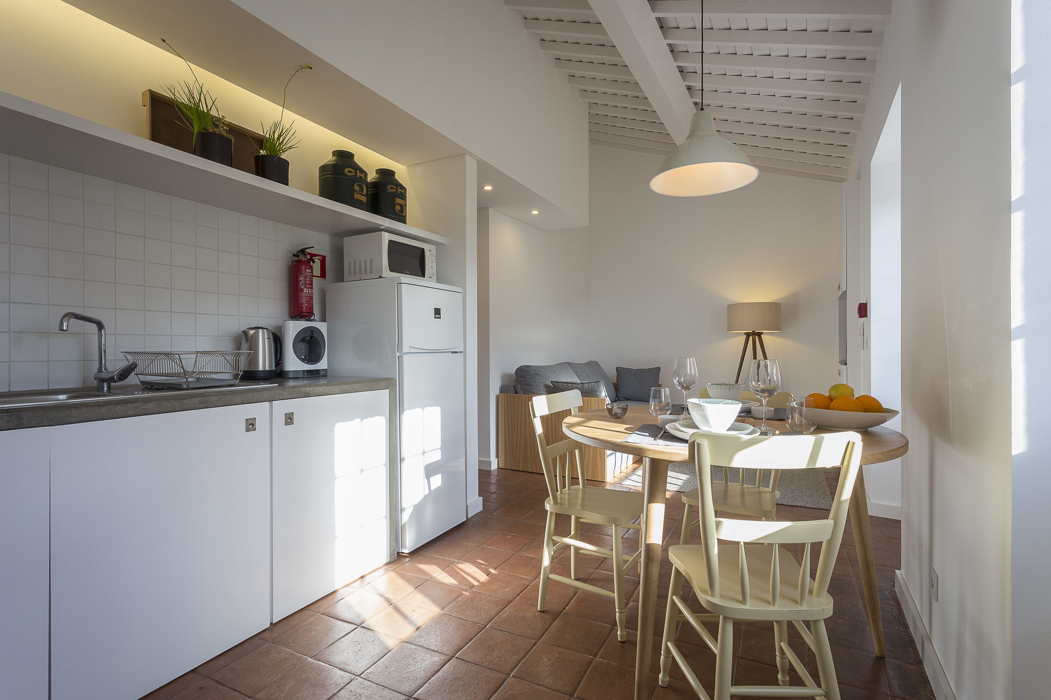 Uma cozinha moderna com armários brancos, uma mesa de jantar com cadeiras e teto com vigas aparentes.