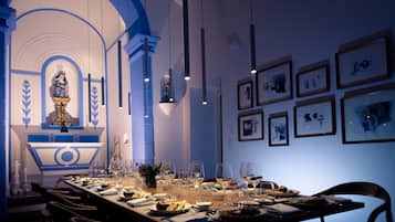 Un comedor con una larga mesa dispuesta para una comida, obras de arte enmarcadas en las paredes y una estatua al fondo.