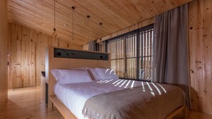 Ein Schlafzimmer mit Holzwänden, einem Bett, großen Fenstern und hängenden Leuchten.
