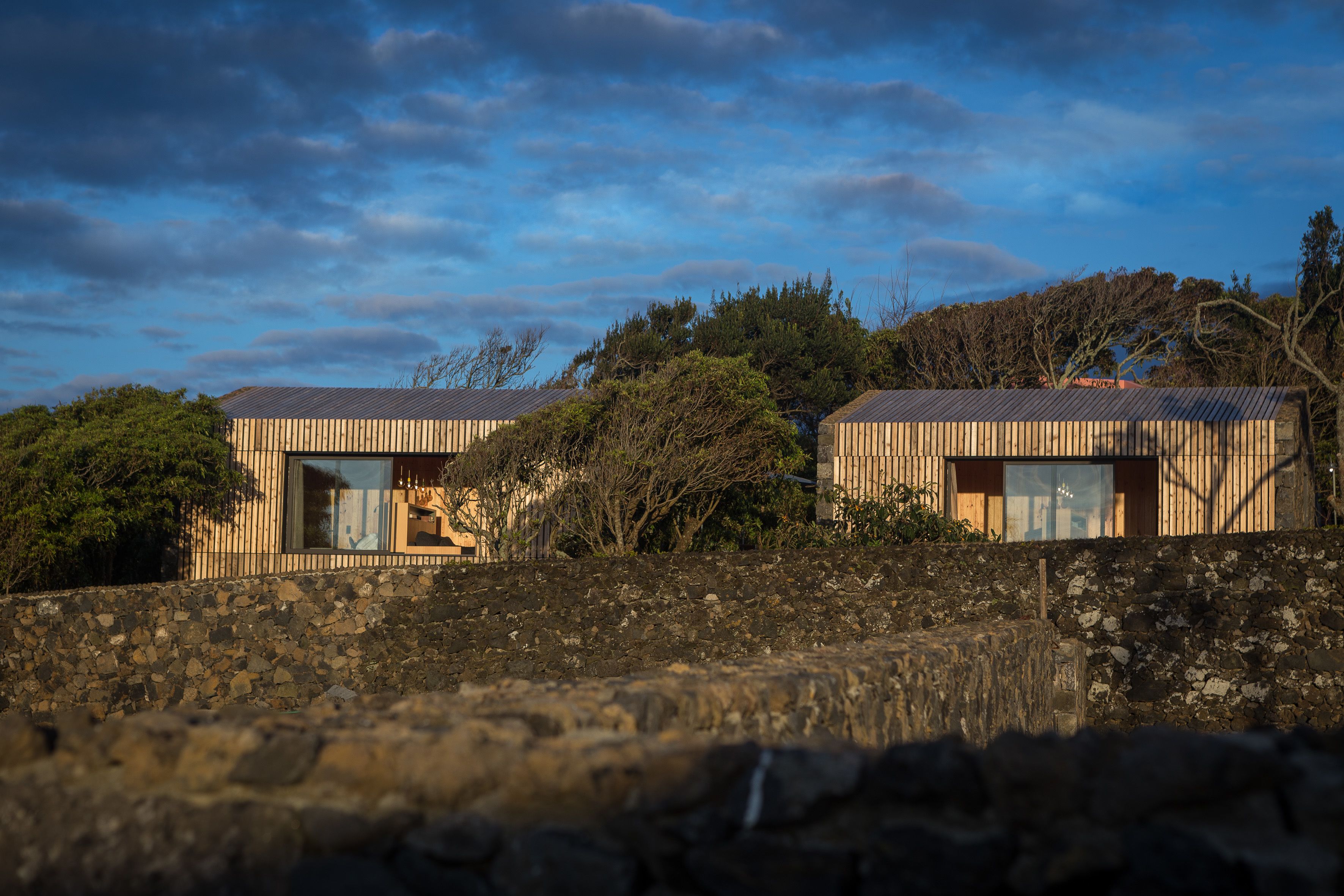 Dos casas modernas con ventanas amplias y un muro de piedra al frente.