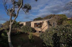 Una casa moderna con fachada de madera, rodeada de exuberante vegetación y un cielo despejado.