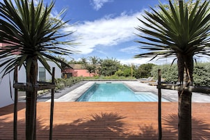 Piscina rectangular con cubierta de madera al frente, rodeada de palmeras y cielo despejado.