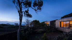 Ein modernes Haus mit einem großen Panoramafenster, umgeben von Bäumen und einem Garten.