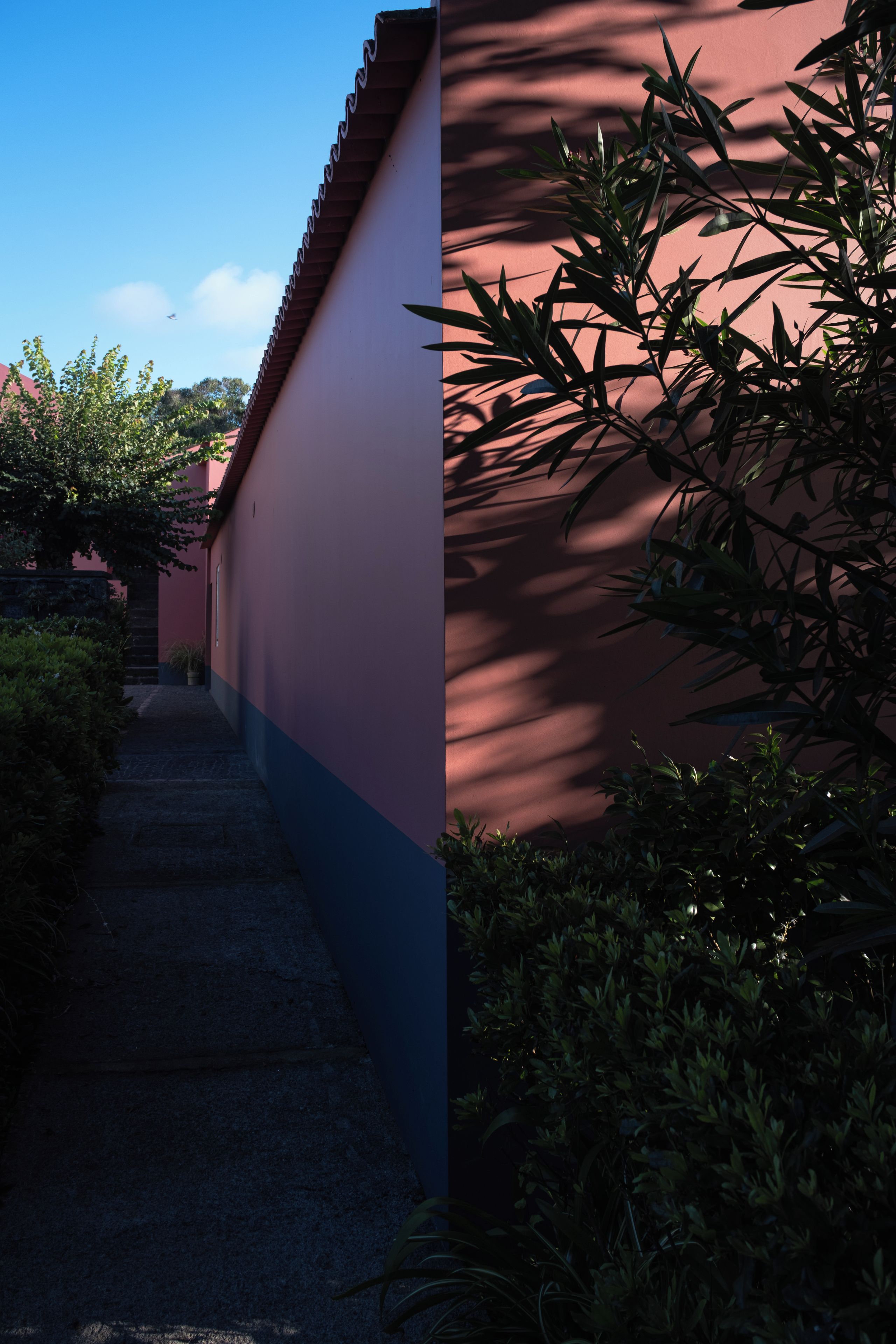 Um caminho estreito que leva a um edifício com parede vermelha e telhado em telhas.