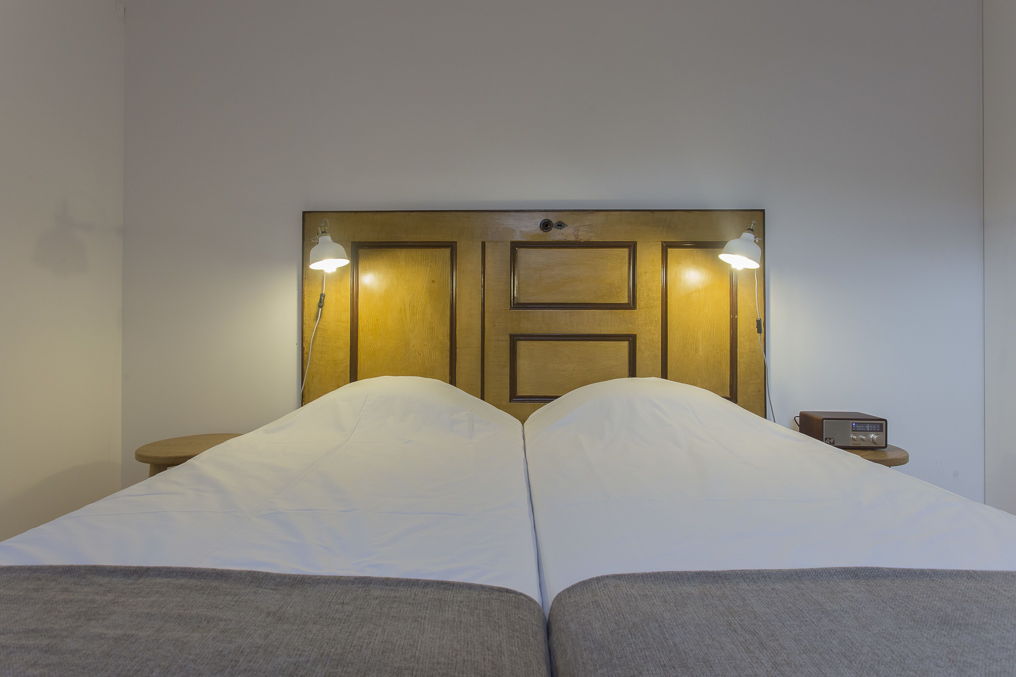 A double bed with two pillows, a bedside table with a radio, and a wooden headboard with two wall-mounted lights.