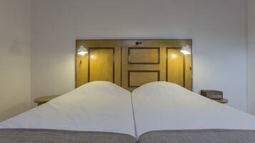 A double bed with two pillows, a bedside table with a radio, and a wooden headboard with two wall-mounted lights.