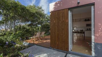 A modern house with a wooden deck, a sliding glass door leading to a kitchen, and a garden with plants and a patio.