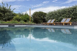 Une piscine à l’eau claire, entourée de verdure et de chaises longues en bois.