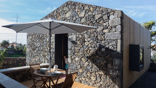 Ein Steinhaus mit einer Holzterrasse, Sitzgelegenheiten im Freien und einem großen Sonnenschirm.