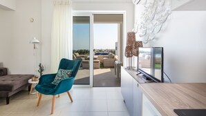Ein modernes Wohnzimmer mit einem türkisfarbenen Sessel, einer Couch, einem Fernseher und Blick ins Freie.