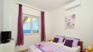 Un dormitorio con cama, televisor, ventana con cortinas, un cuadro y aire acondicionado.