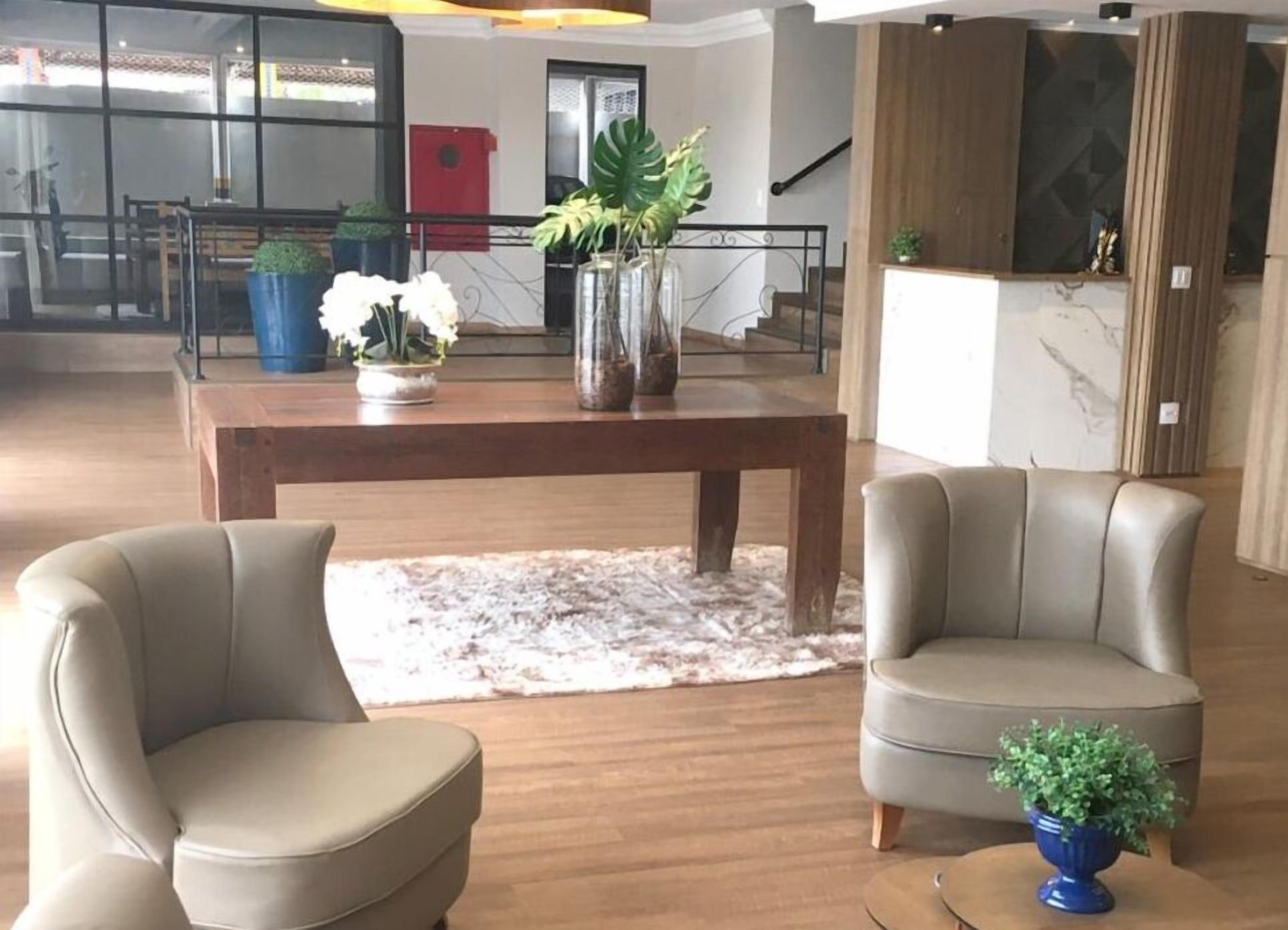 A spacious living area with a wooden table, two leather armchairs, a shaggy rug, and potted plants.