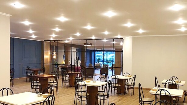 Un comedor amplio con varias mesas y sillas, un ventanal que ofrece vistas al exterior, y un diseño moderno de techo con iluminación empotrada.