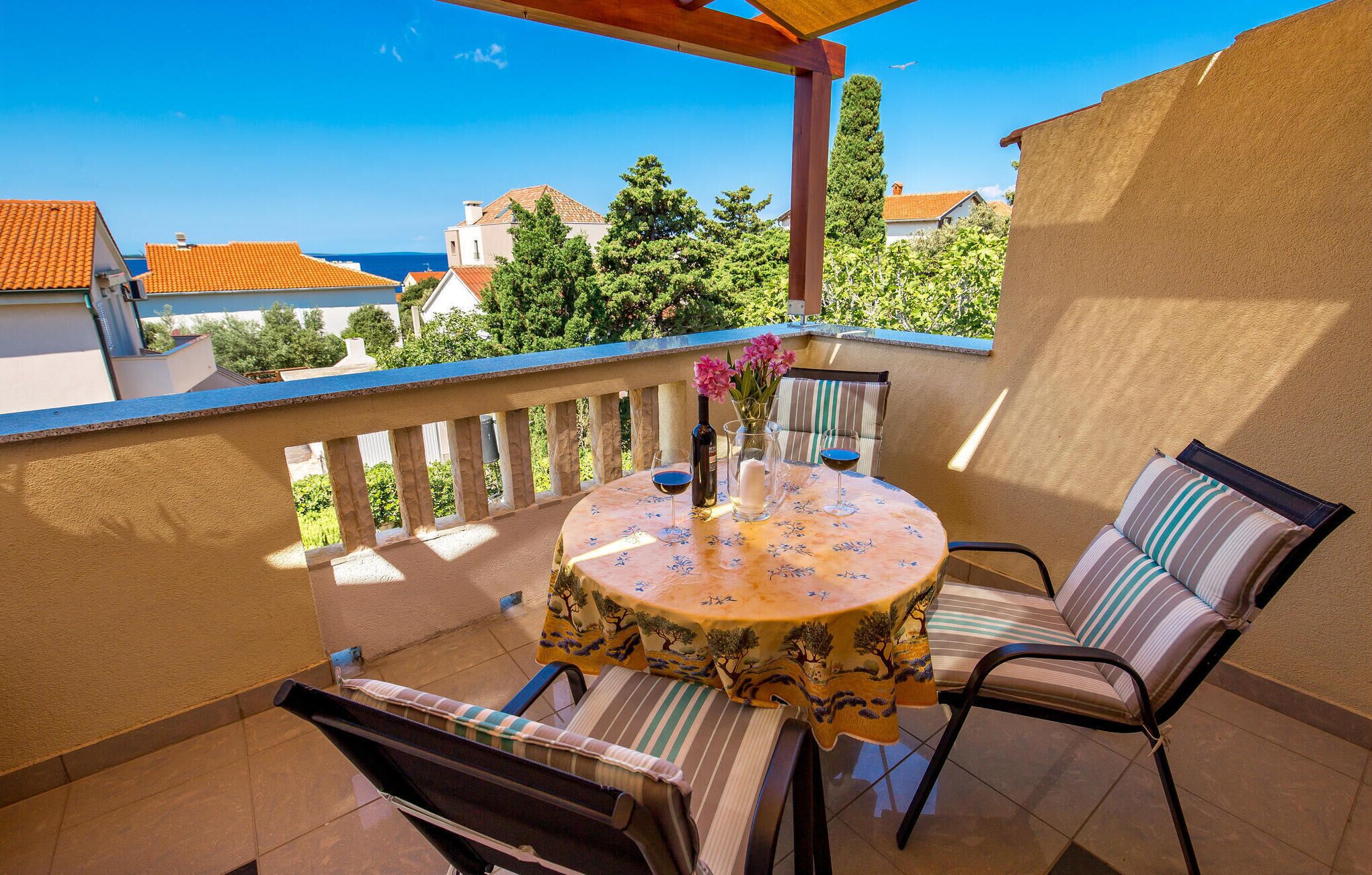 A balcony with a round table, two chairs, a vase with flowers, and a bottle of wine.