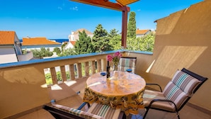 Ein Balkon mit rundem Tisch, zwei Stühlen, einer Blumenvase und einer Weinflasche.