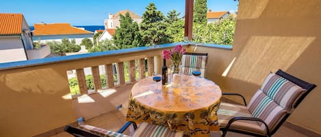 A balcony with a round table, two chairs, a vase with flowers, and a bottle of wine.